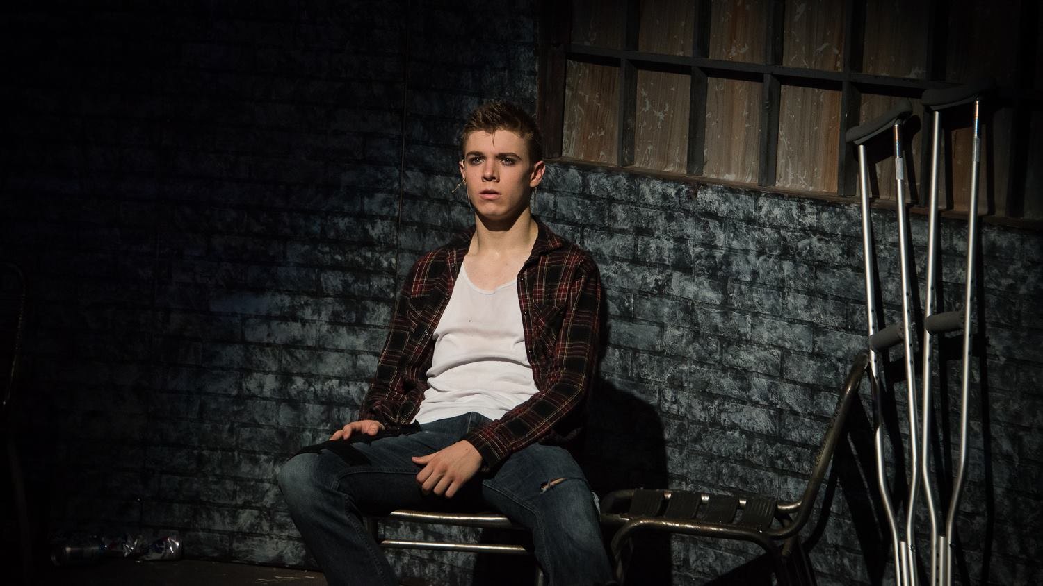 Johnny seated against the brick wall with crutches