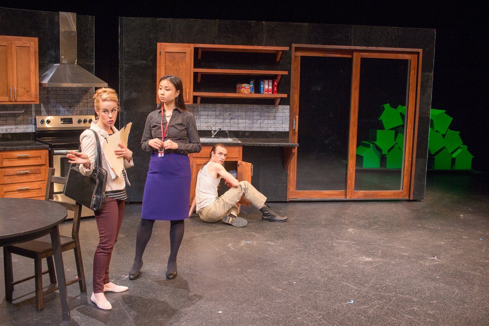Production photo — three characters in the kitchen