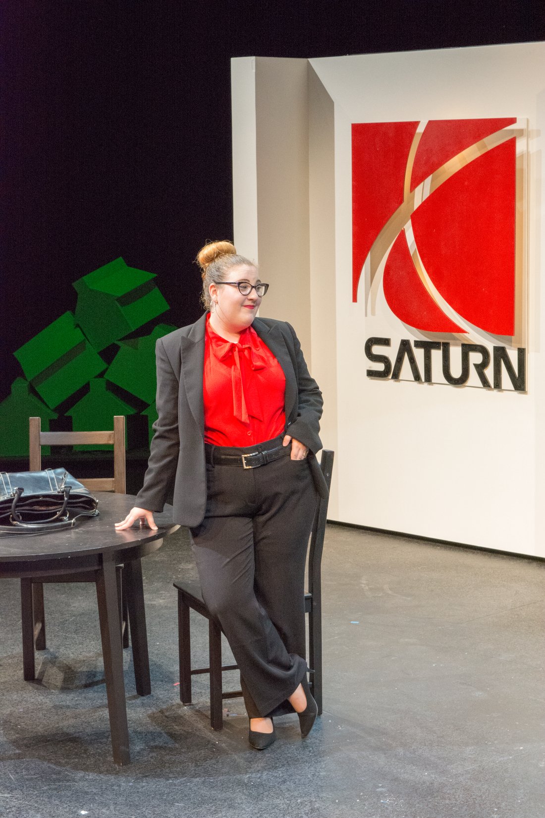 Production photo — a character seated before the Saturn dealership sign