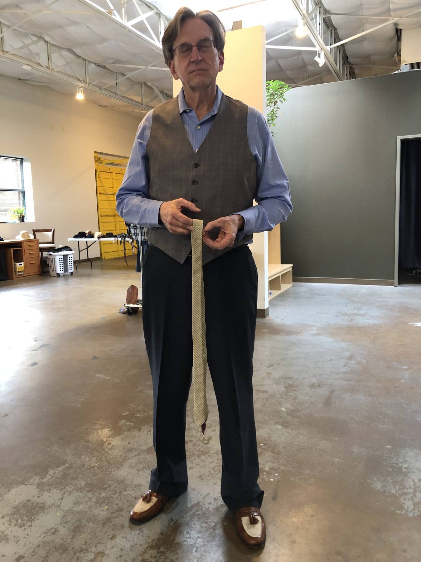 Character fitting — tweed vest over blue dress shirt, navy trousers, two-tone loafers