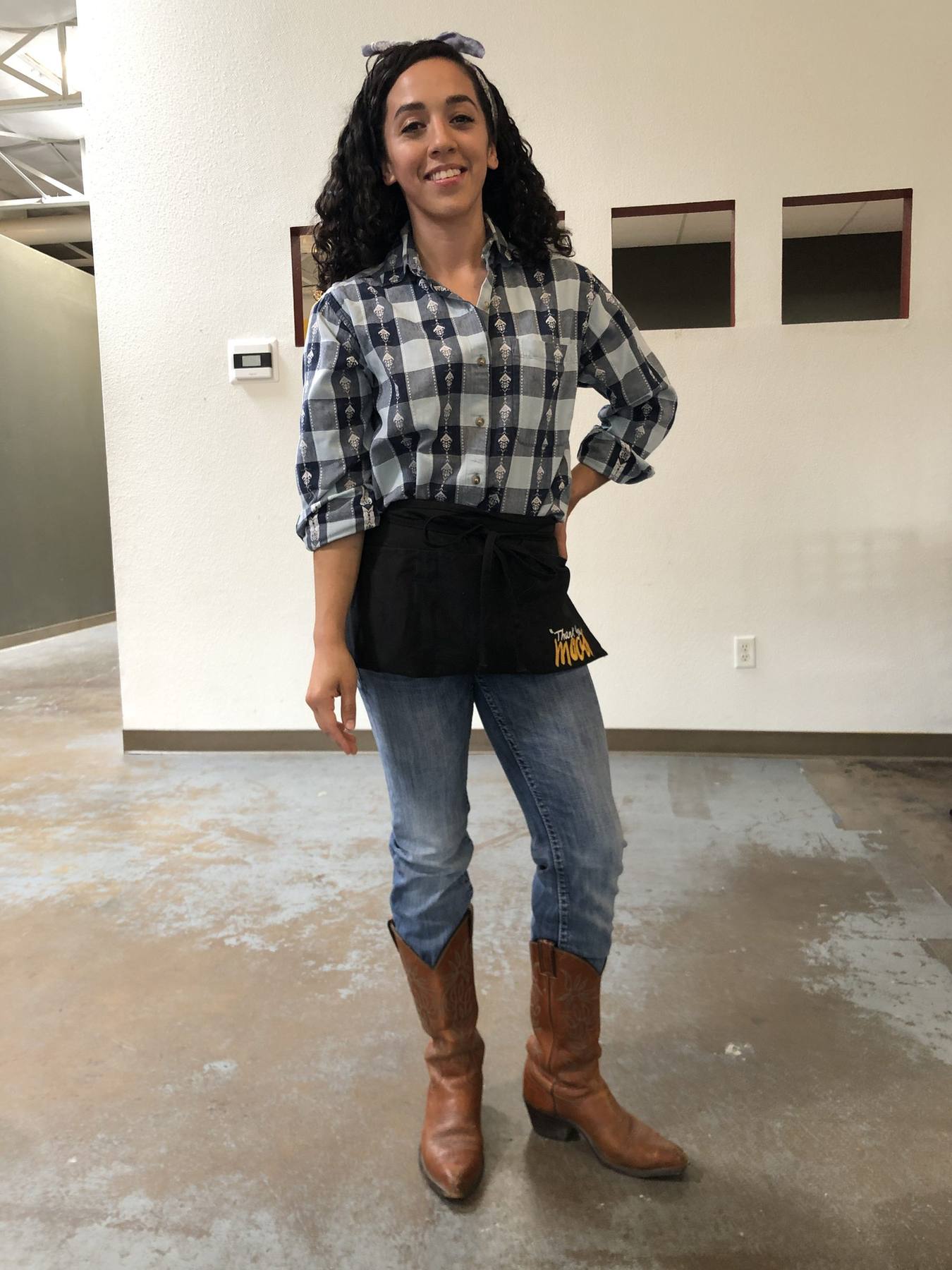 Character fitting — plaid shirt, branded half apron, jeans, tan cowboy boots