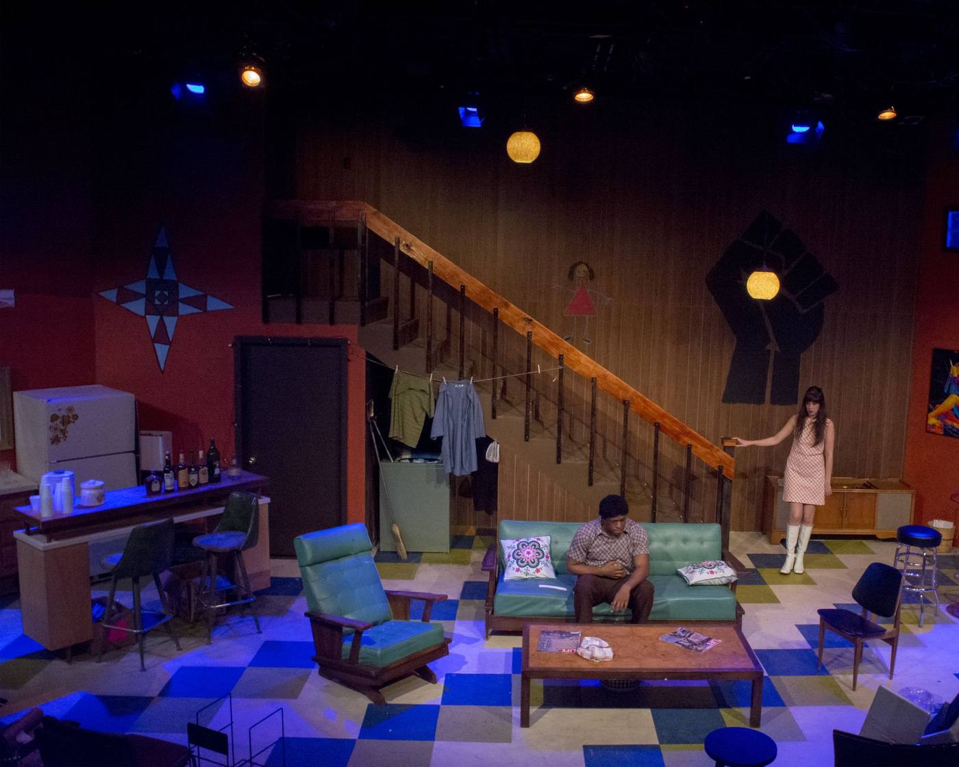 Production photo — full set with actors, staircase and fist mural