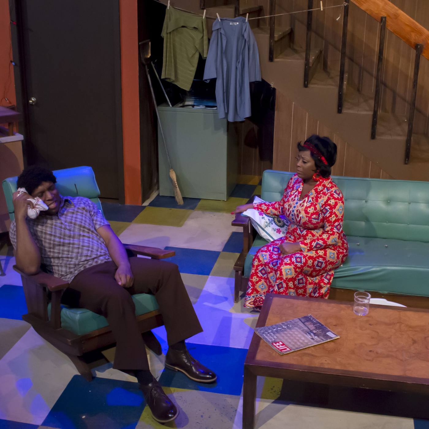 Production photo — two characters on the sofa, emotional scene