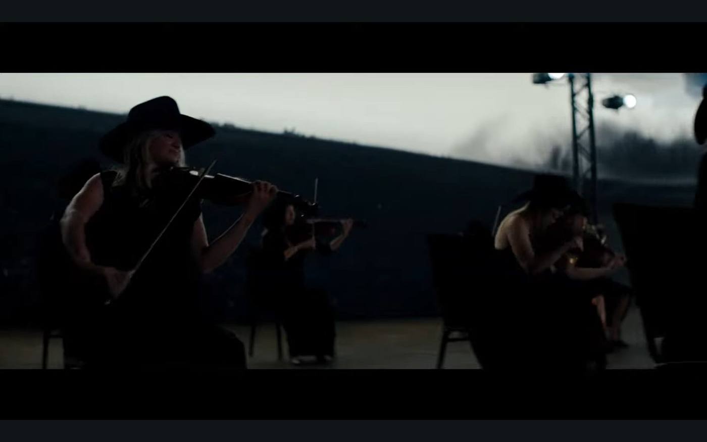 Final still — string section in cowboy hats, all-black wardrobe with silhouette read