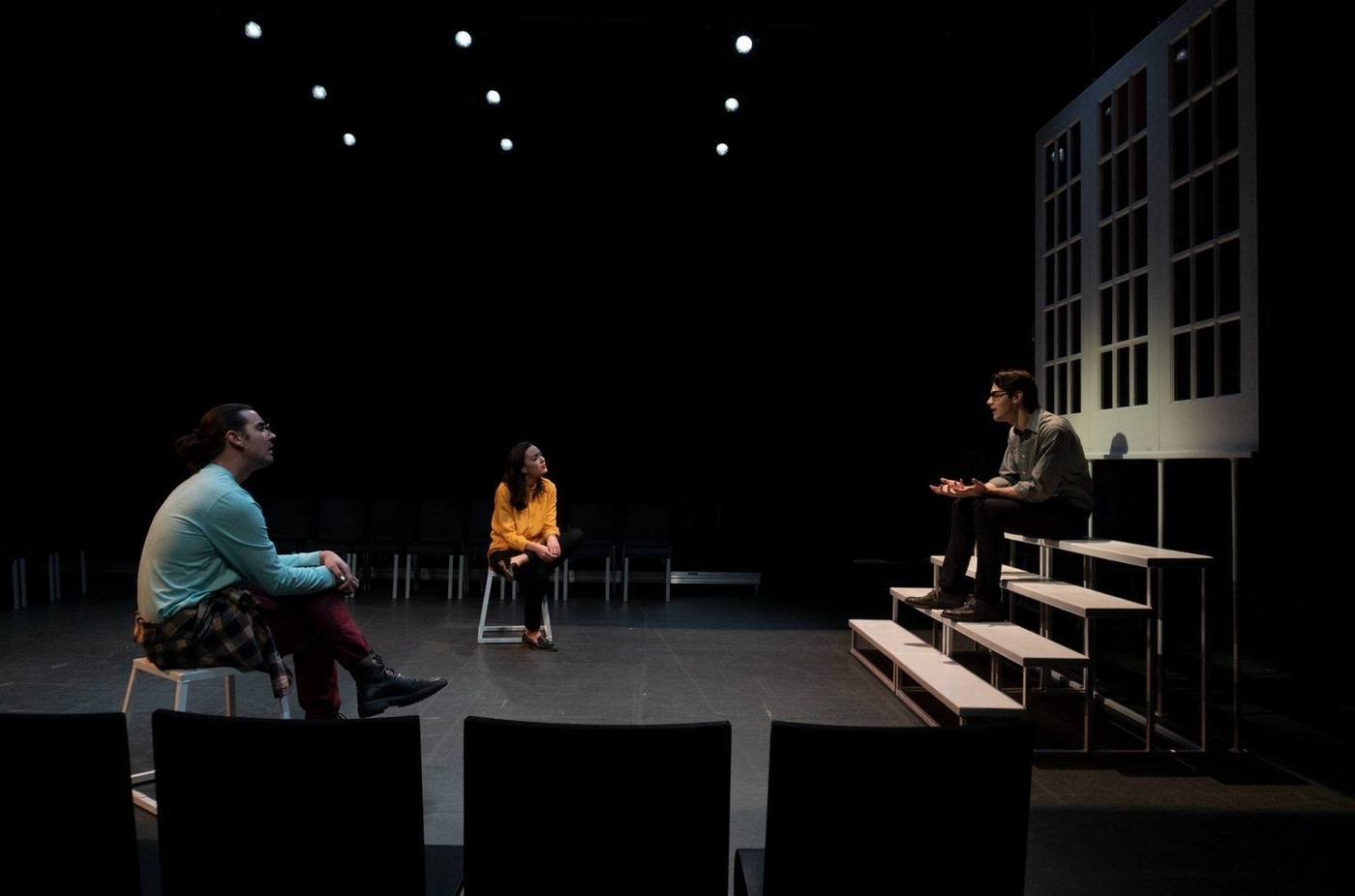 Production — actors seated on stools and the step unit in a scene caught in window-pattern light