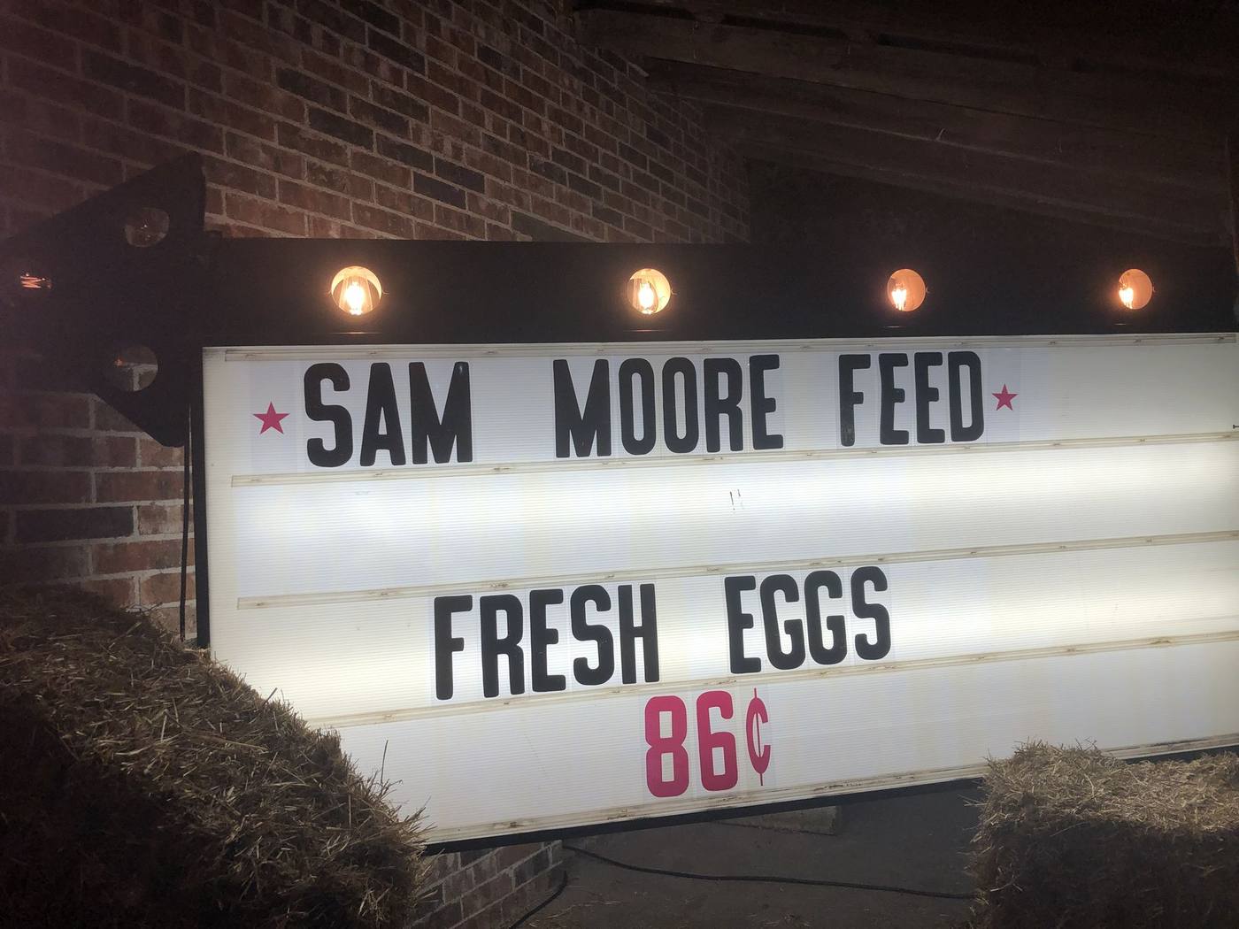 Sam Moore Feed sign lit at night with hay bales
